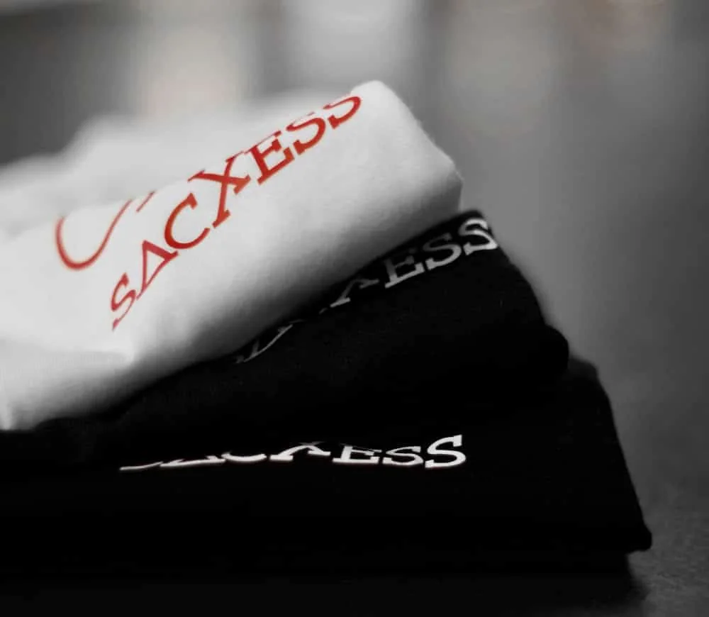 Folded white and black tees showing the printed SACXESS wordmark